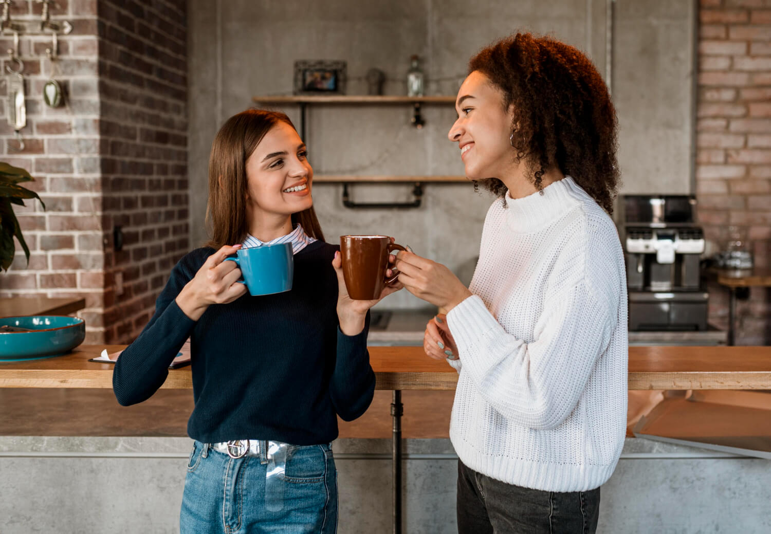 Duas amigas sorridentes conversando e bebendo café em canecas, ilustrando os cuidados com o clareamento dental no Instituto do Sorriso em Vila Maracanã.