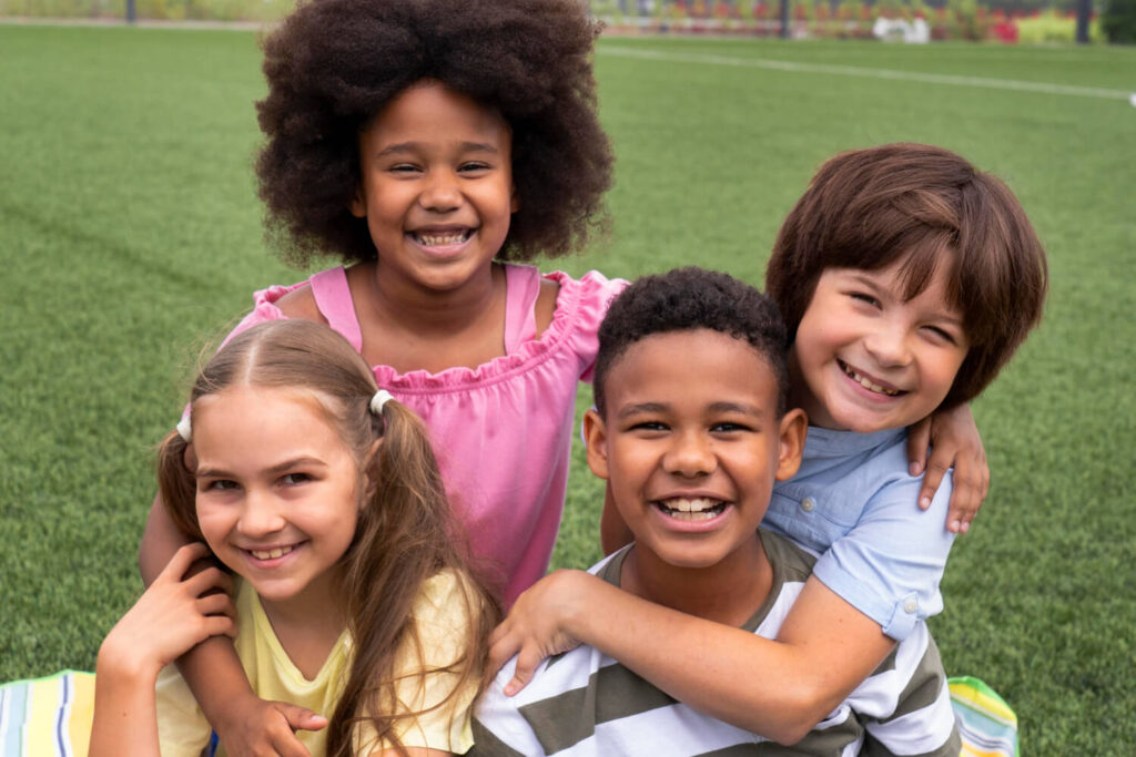 Quatro crianças sorrindo em um gramado. Opção de aparelho alinhador invisível infantil no Instituto do Sorriso, na Estrada de Itapecerica.