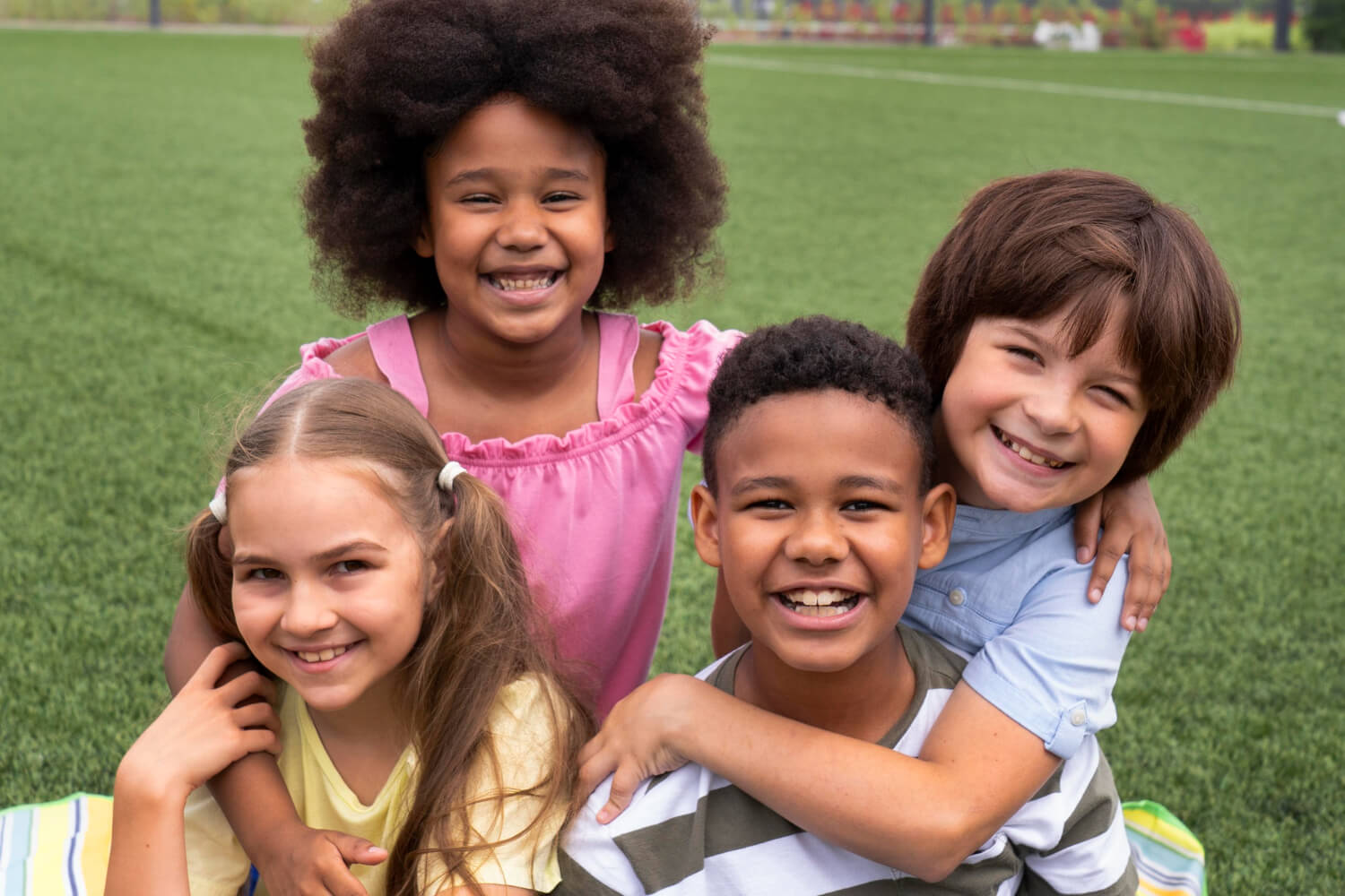 Quatro crianças sorrindo em um gramado. Opção de aparelho alinhador invisível infantil no Instituto do Sorriso, na Estrada de Itapecerica.