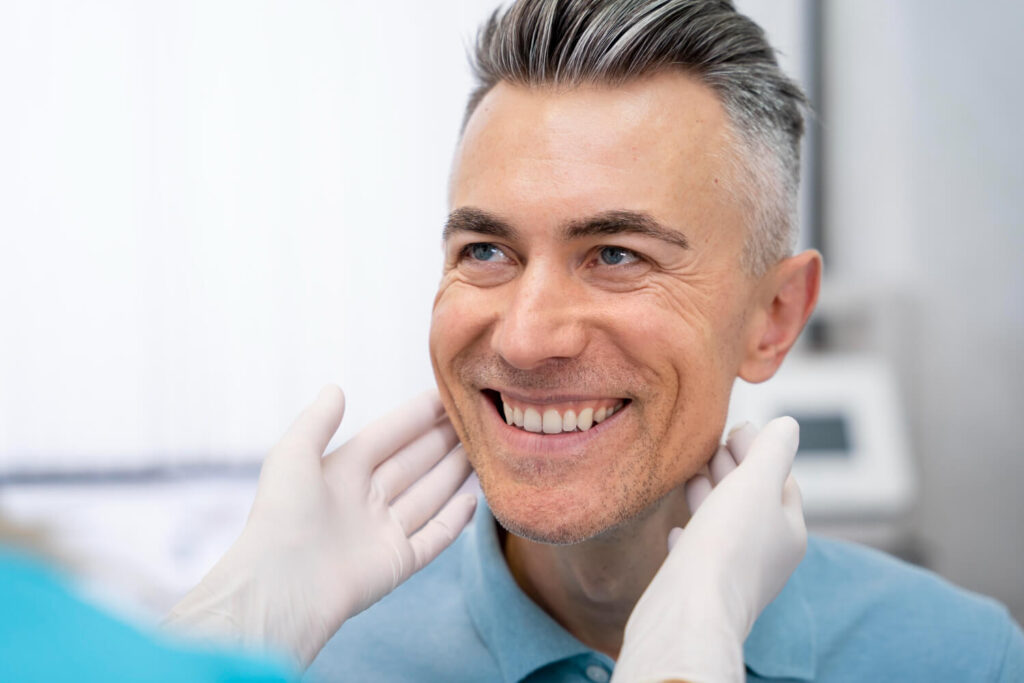 Homem grisalho sorrindo durante avaliação para tratamento de prótese protocolo com dentista na Vila Maracanã.